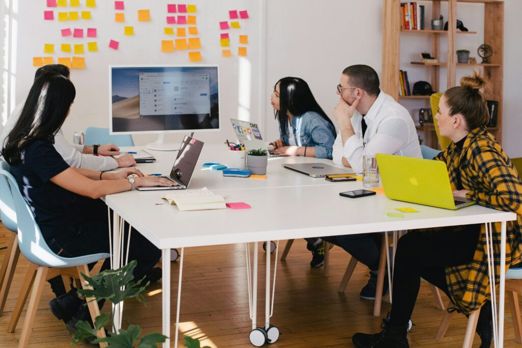 group of people sitting on a table staring at a whiteboard with sticky notes